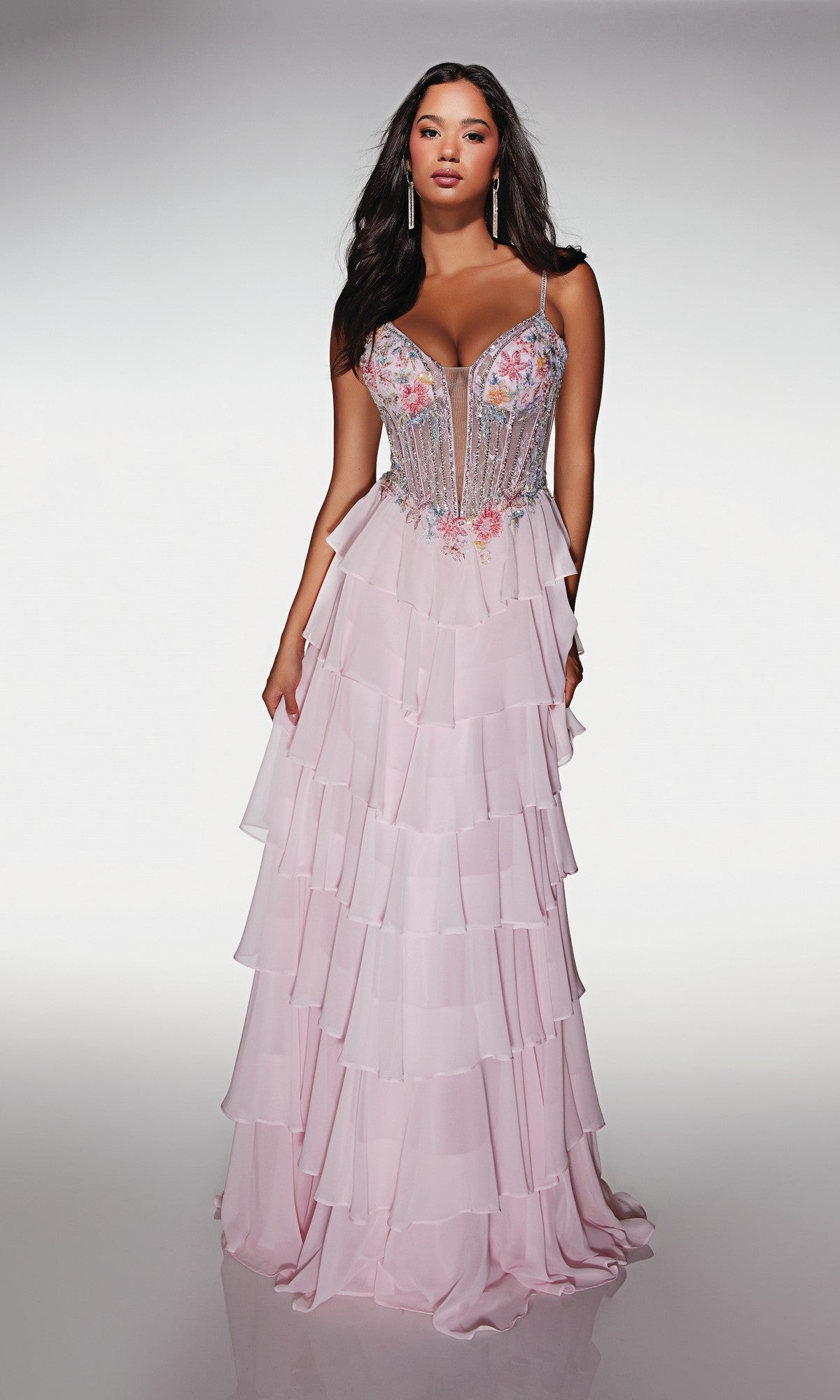 A woman poses in the Alyce 61993 long prom dress in Rosewater, featuring a floral corset bodice with thin straps and a pastel chiffon tiered ruffle skirt, set against a plain background.